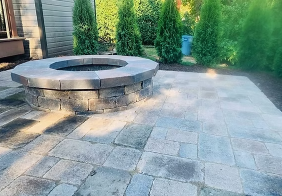 Custom paver patio with stone fire pit surrounded by arborvitae